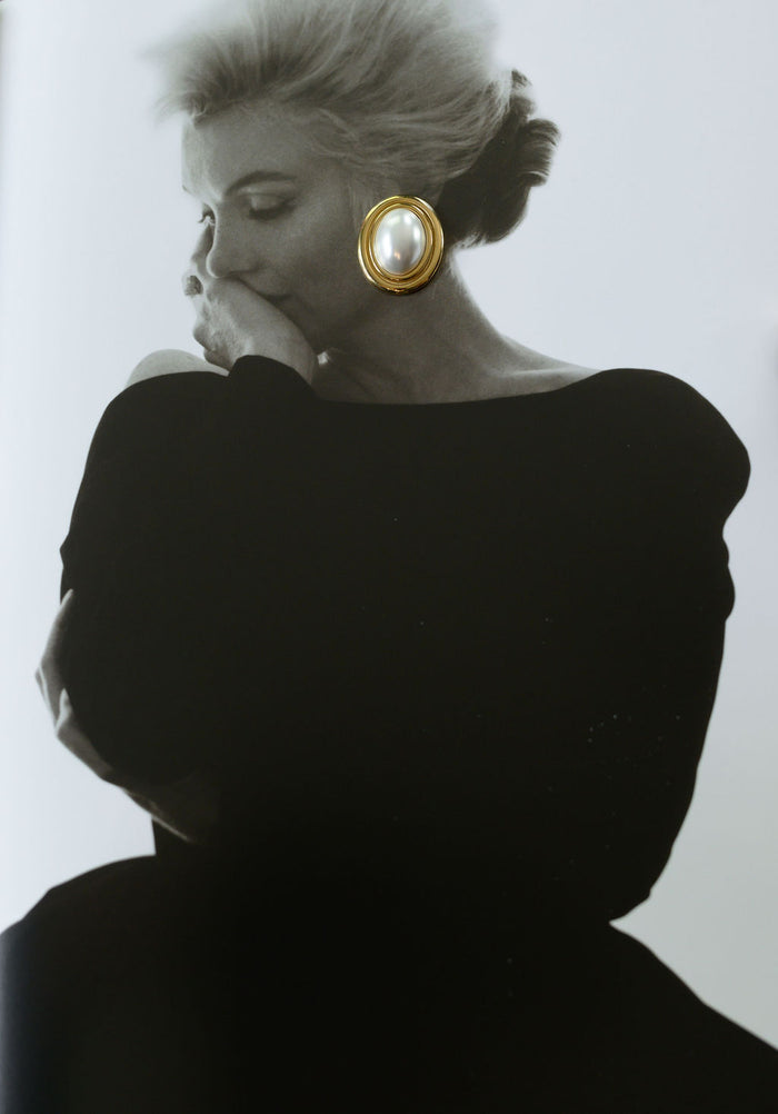 A vintage black and white photograph of a woman with a white and gold earring on top