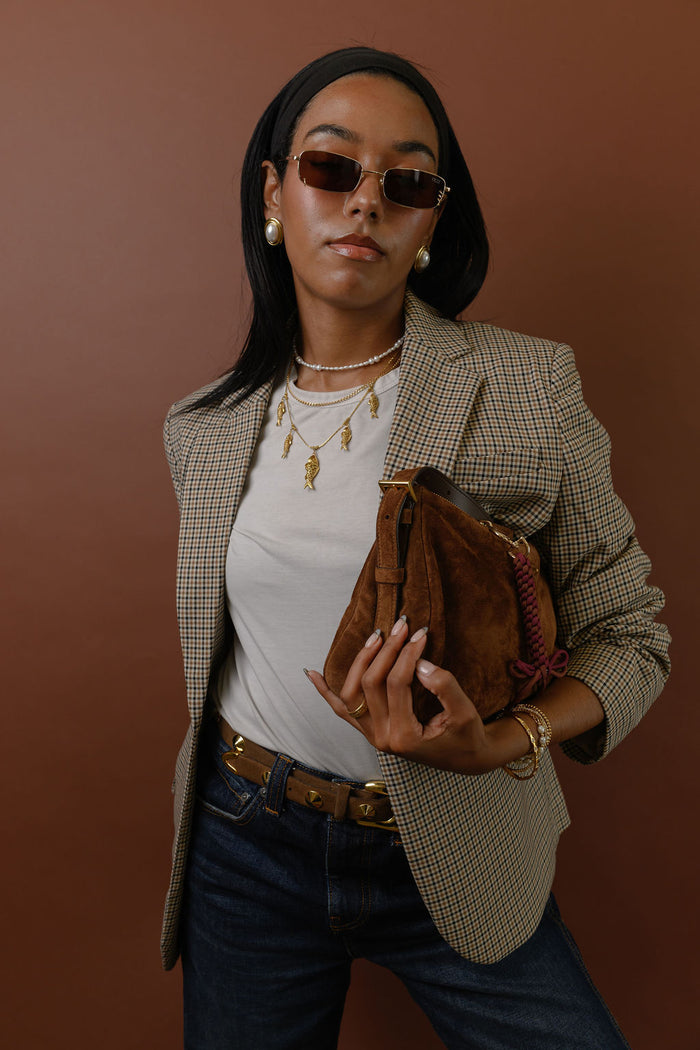 A woman wearing sunglasses, gold accent earrings and necklaces on a red background