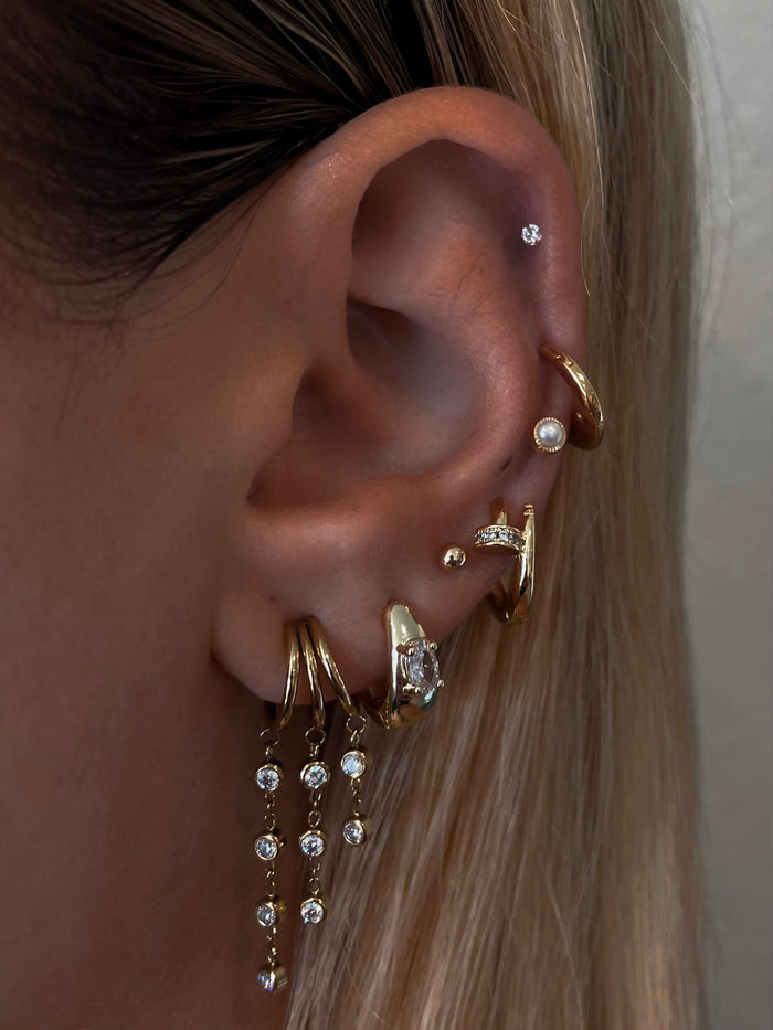 Close-up of an ear with multiple gold and crystal earrings against a neutral background