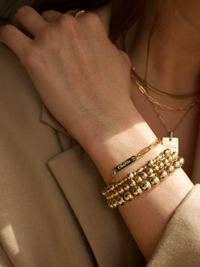 Close up of a person wearing a tan blazer, gold bracelets, and gold necklaces