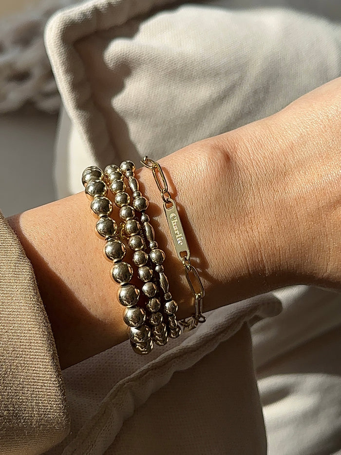 A wrist with a blazer and assorted gold bracelets on a tan background