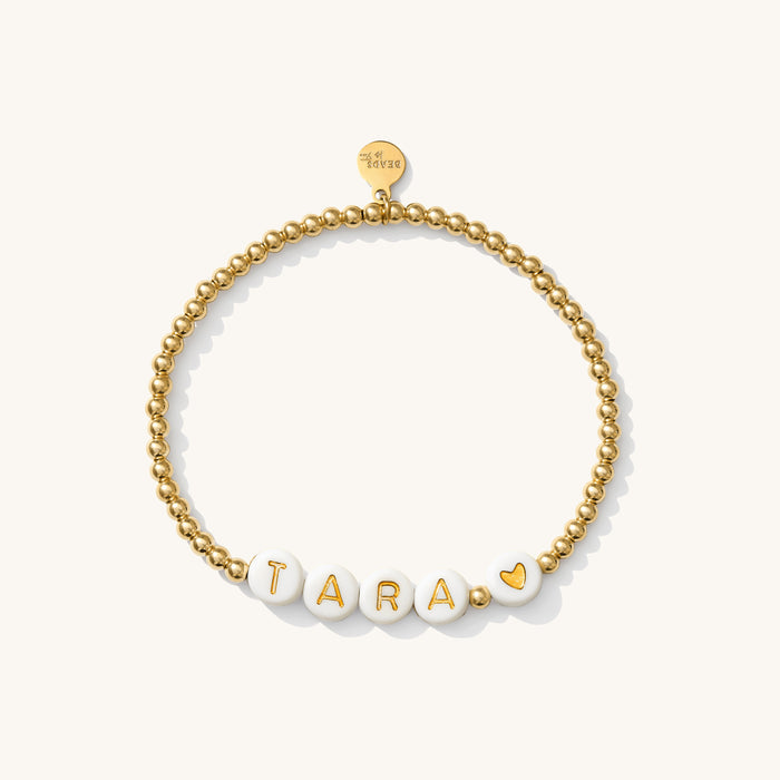 Close up of a gold bead bracelet with white letter beads reading "TARA"