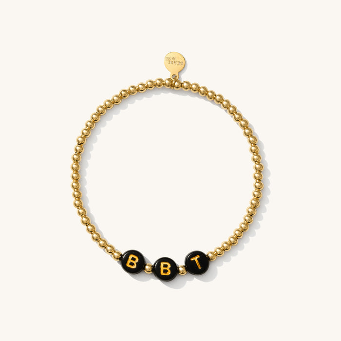 Close up of a gold bead bracelet with black letter beads reading "BBT"