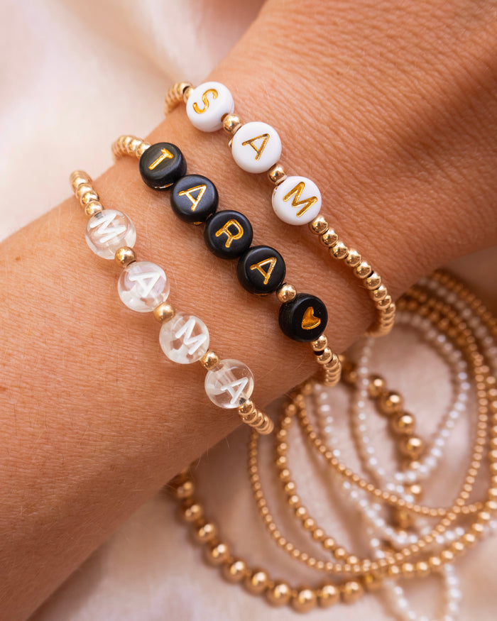 Close up of a wrist with assorted custom bead bracelets, reading "SAM", "TARA <3", and "MAMA"