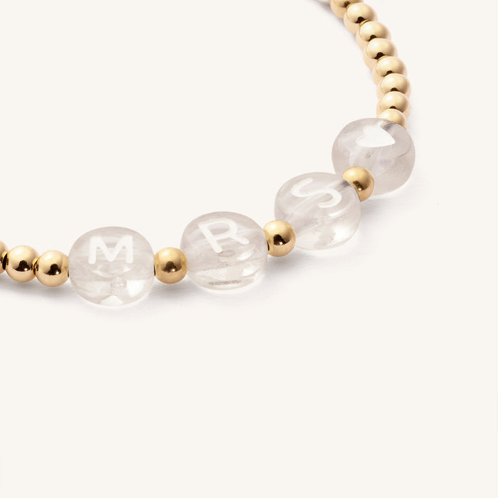 Close up of a gold bracelet with clear beads that say "MRS <3"