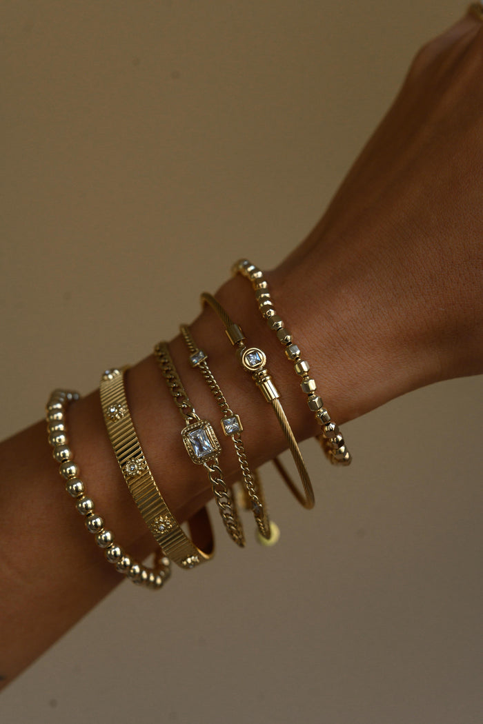 Close up of a wrist with gold bracelets on a neutral background