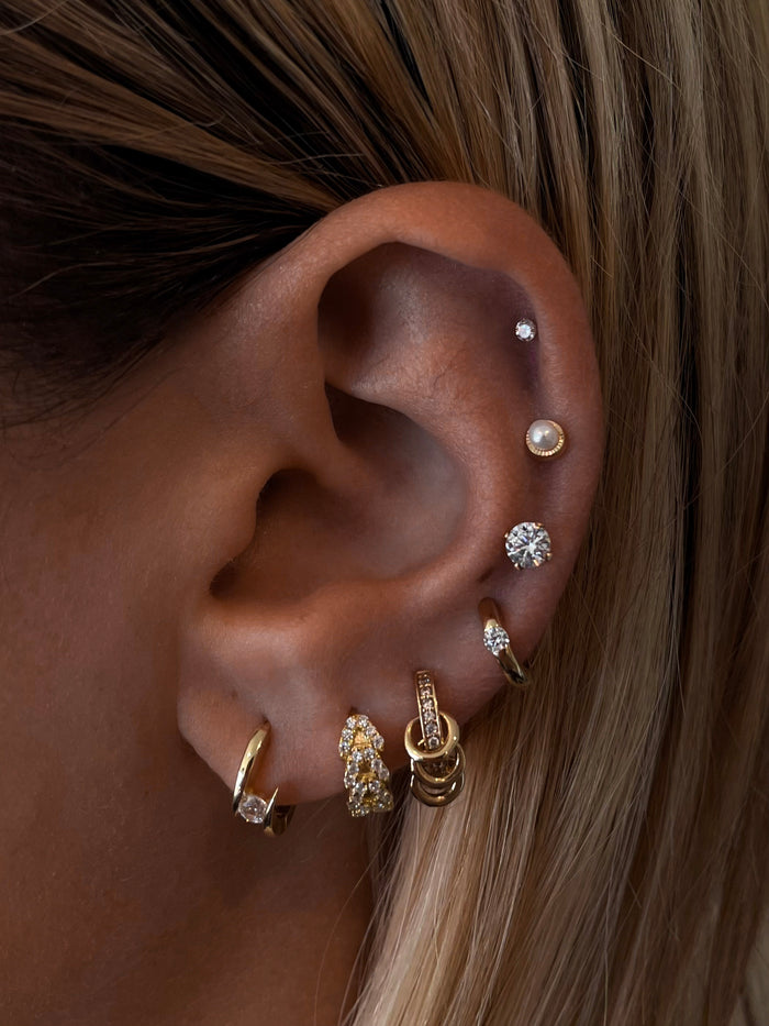Close-up of an ear with multiple gold, pearl, and crystal earrings