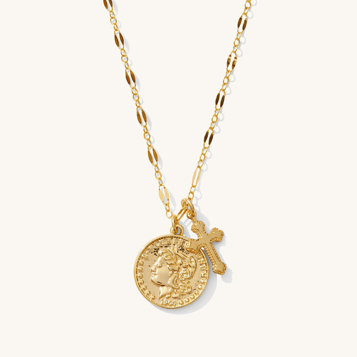 Close up of the gold Desiree cross and coin necklace on a white background