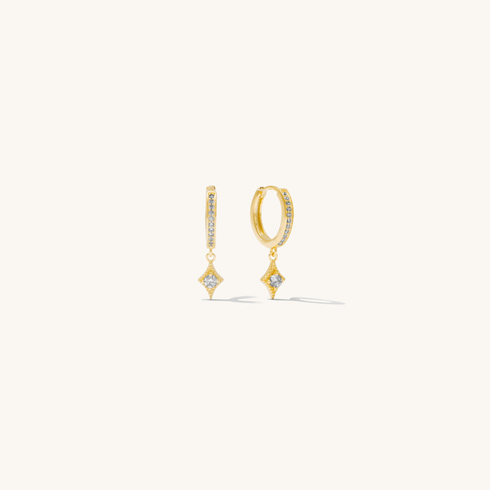 Close-up of huggie earrings with accent stone dangling on a white background
