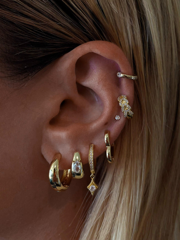 Close-up of an ear with multiple gold and crystal earrings
