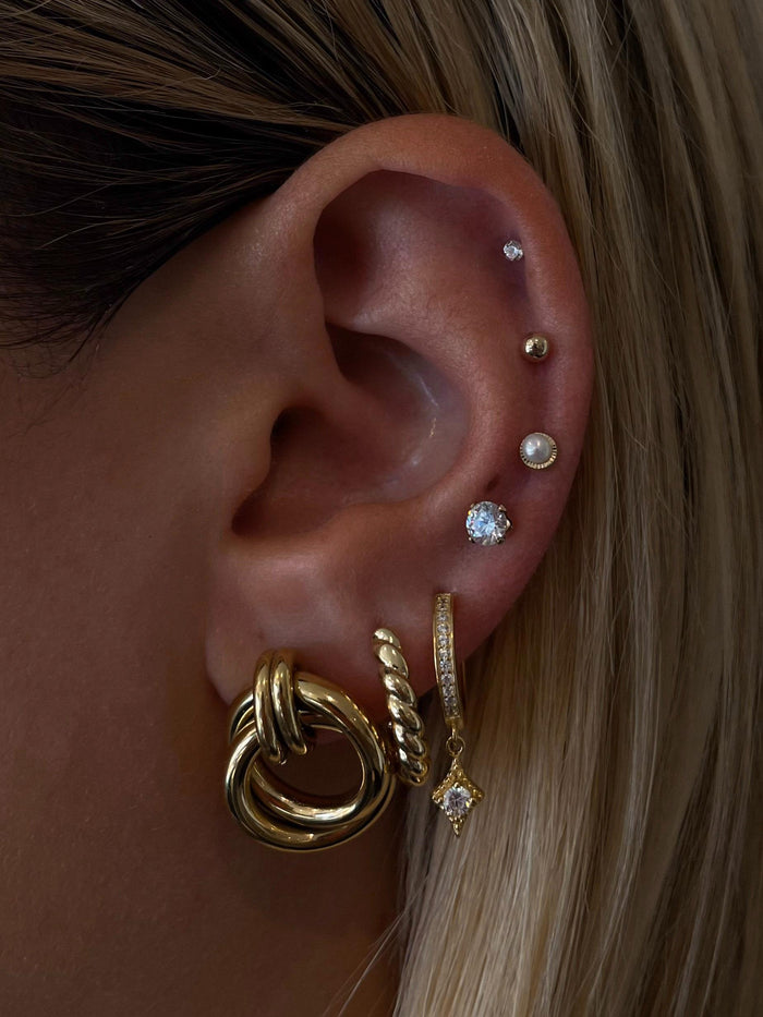 Close-up of an ear with multiple gold, pearl, and crystal earrings
