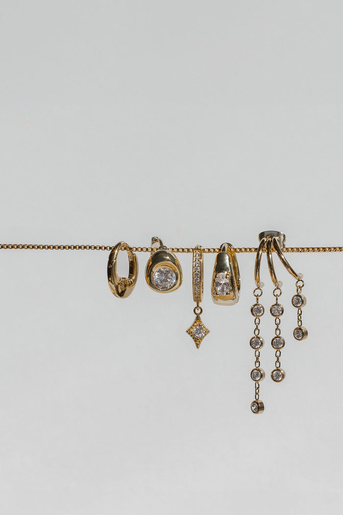 Five unique earrings with stone accents hanging from a gold chain on a white background