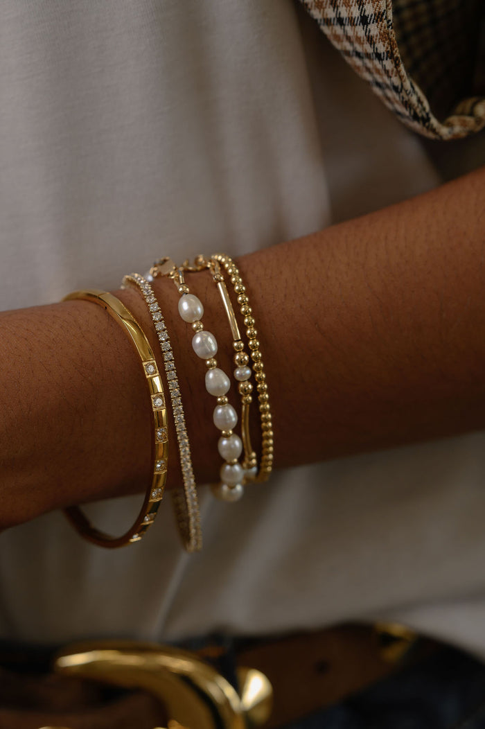 Close up of a wrist with multiple gold and pearl bracelets