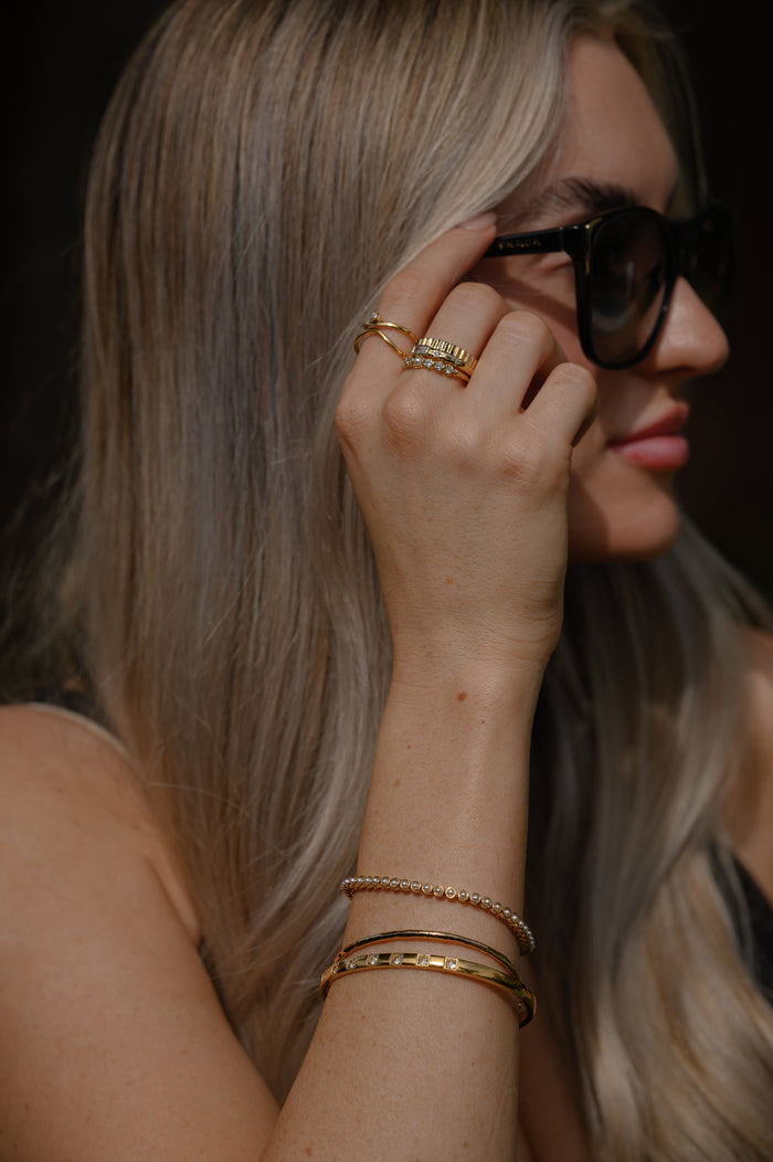 A woman wearing sunglasses, gold rings, and gold bracelets