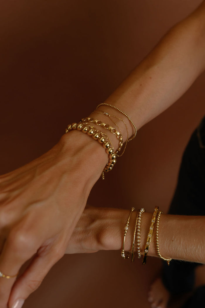 Close up of wrists with gold bracelets on a brown background