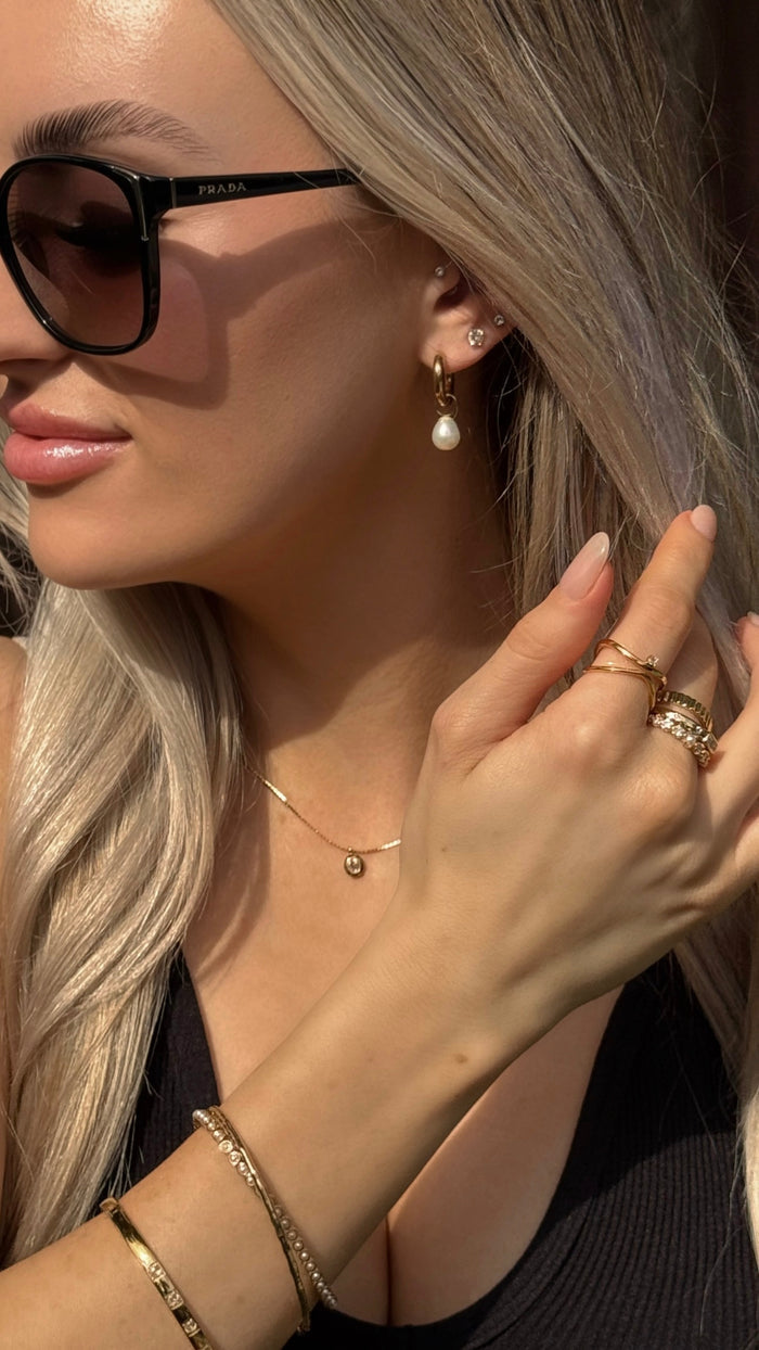 Close up of a woman wearing sunglasses and assorted gold jewelry
