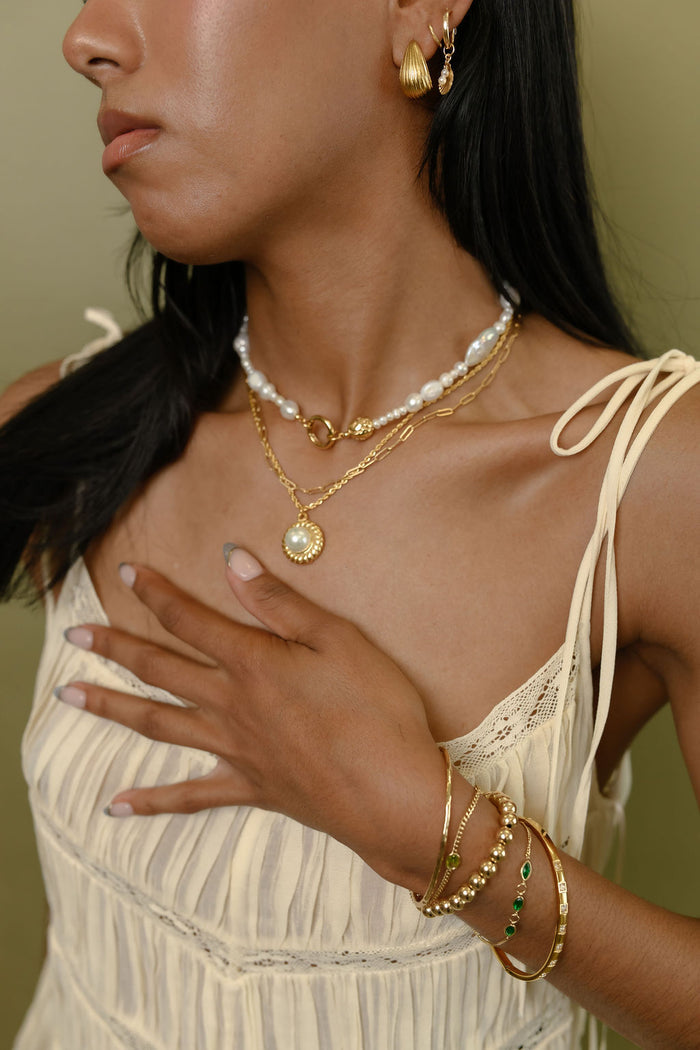 A woman in a white tank top and gold jewelry on a green background