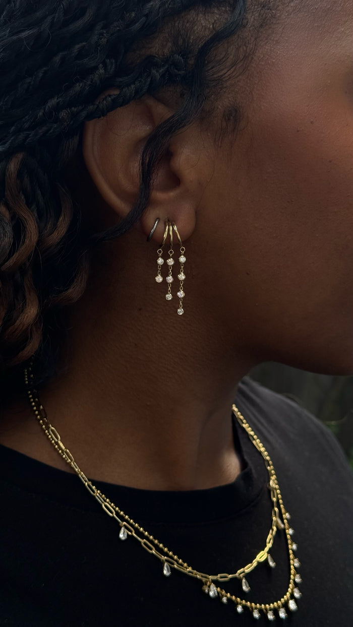Close-up side view of a woman wearing gold earrings, and necklaces in a black shirt