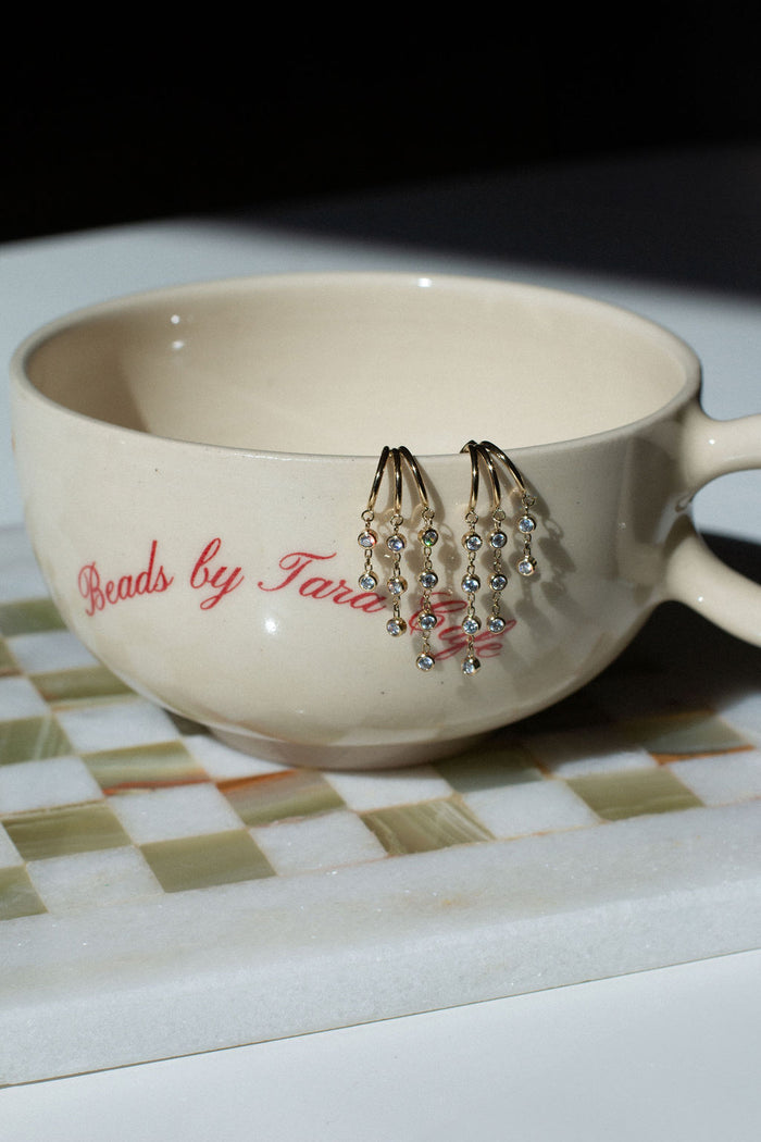 A pair of stone dangle earrings on the edge of a coffee cup on a green checkerboard