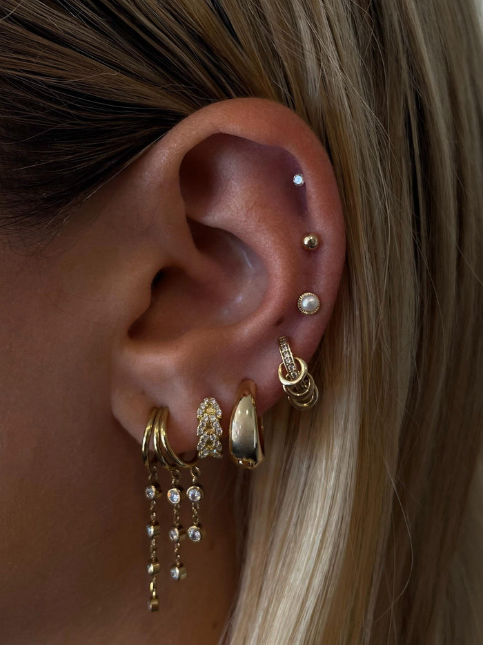Close-up of an ear with multiple gold and crystal earrings