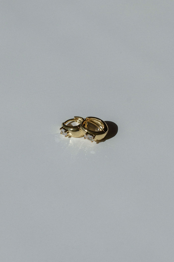 Gold huggie earrings on a neutral background