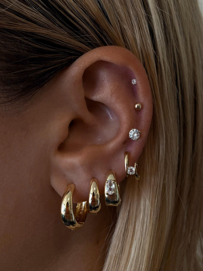 Close-up of an ear with multiple gold and crystal earrings