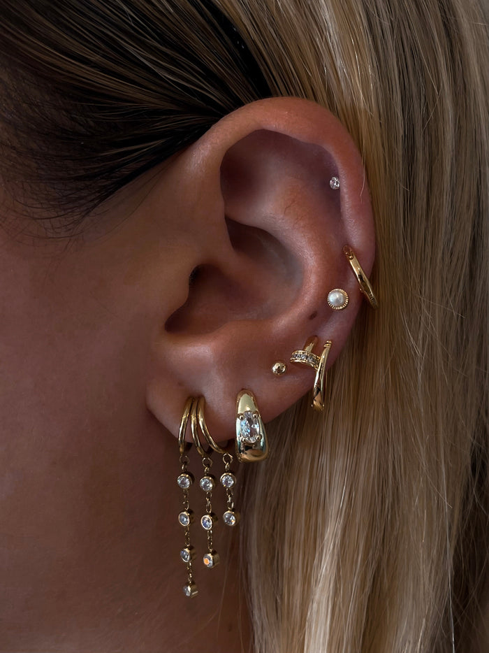 Close-up of an ear with multiple gold and crystal earrings