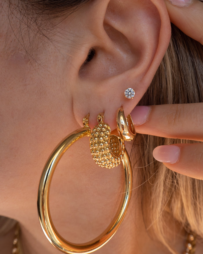 Close-up of an ear with multiple gold and crystal earrings