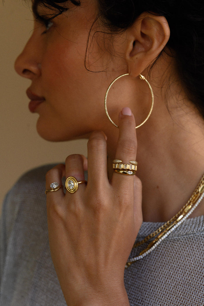 Close-up side view of a woman wearing gold hoops, rings, and necklaces in a grey sweater