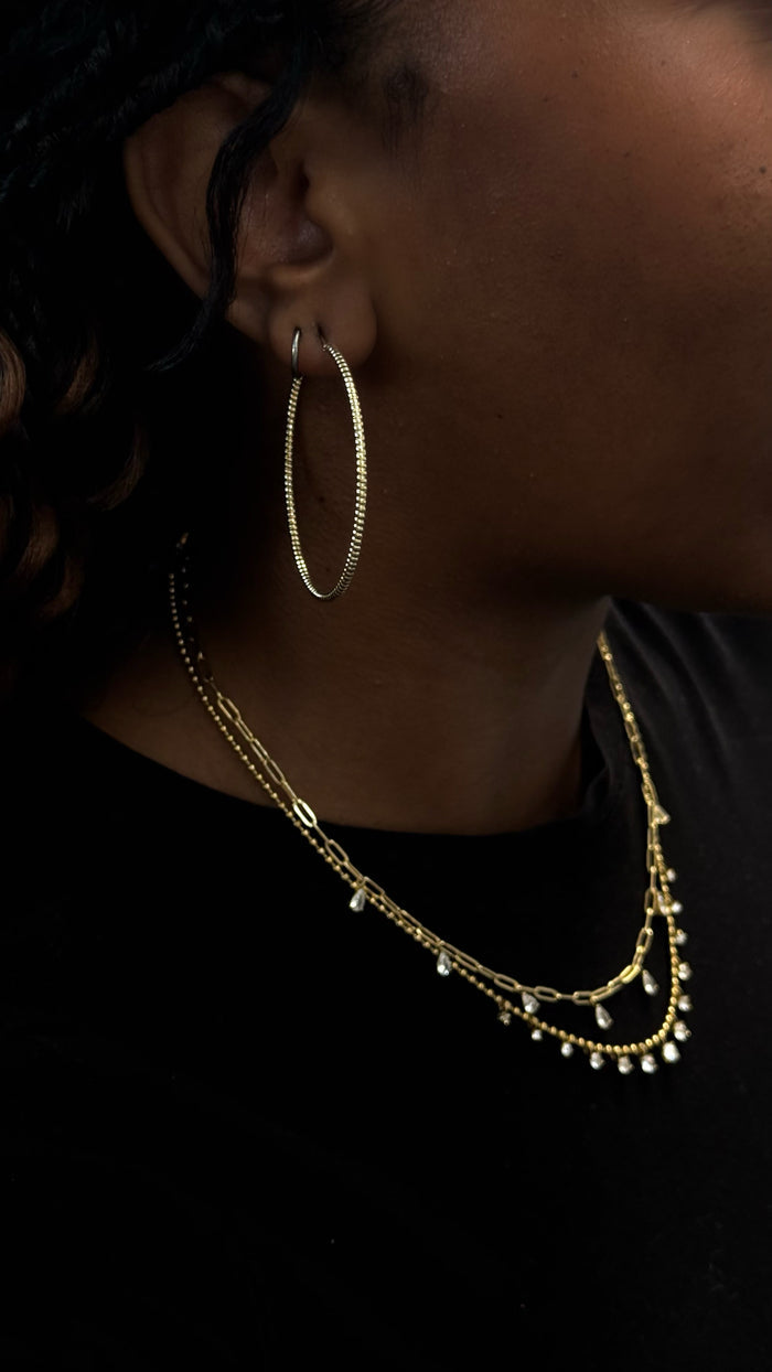 Close-up side view of a woman wearing gold hoops and necklaces in a black shirt