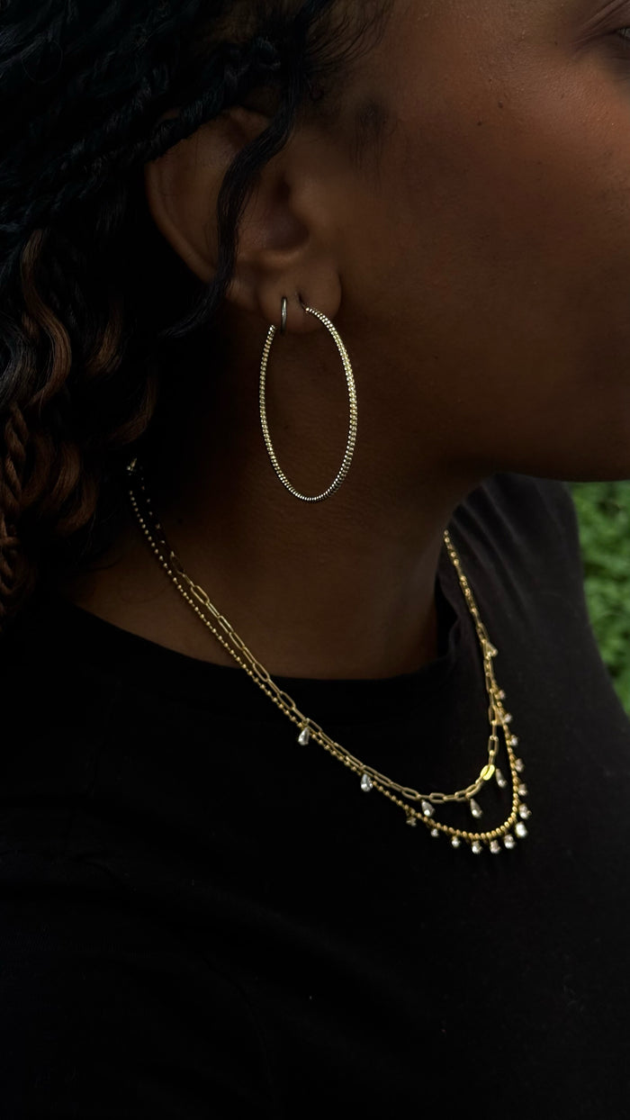 Close-up side view of a woman wearing gold hoops and necklaces in a black shirt
