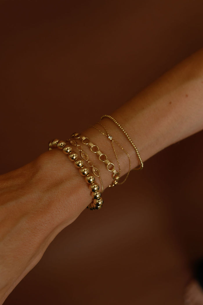 Close up of a wrist with gold jewelry on a brown background