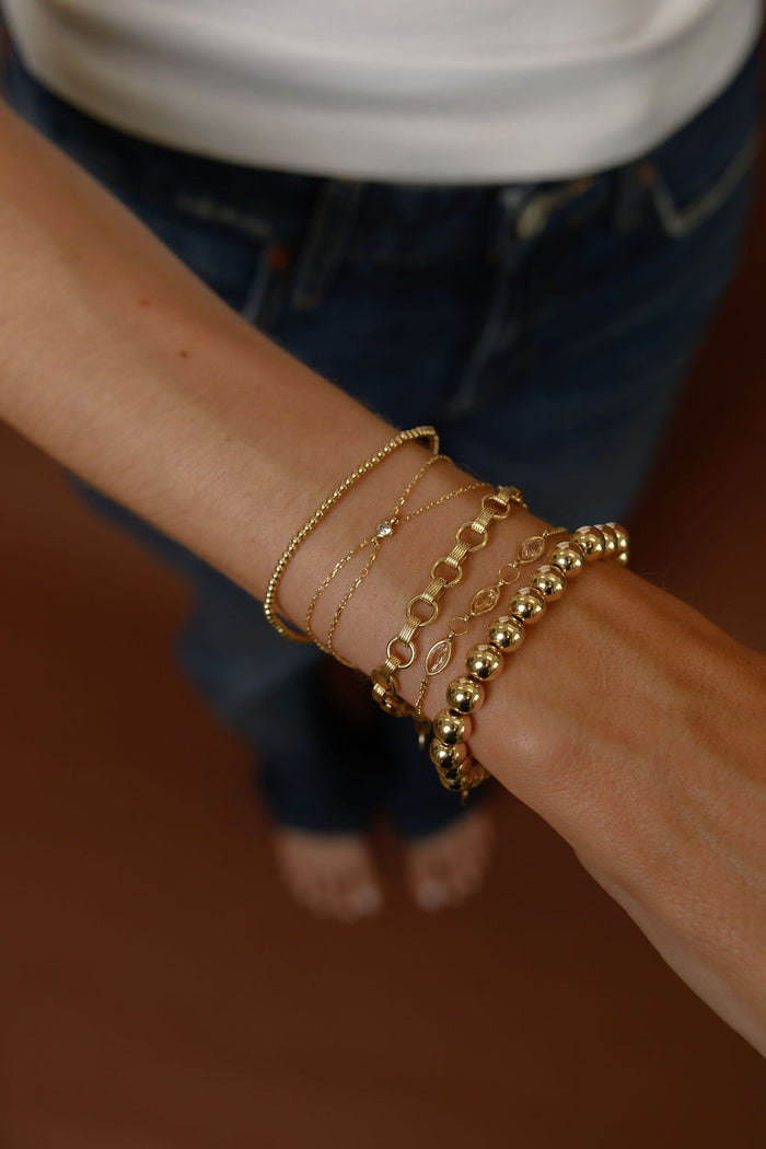Close up of a wrist with gold bracelets on a brown background