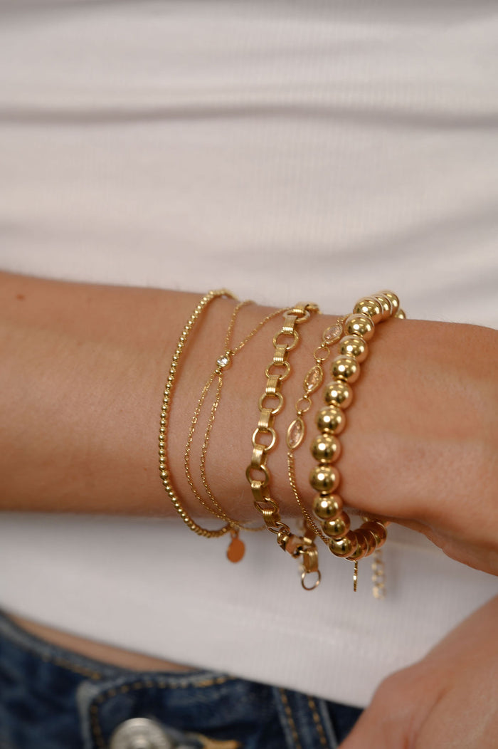 Close up of a person wearing gold bracelets, a white tank top, and blue jeans