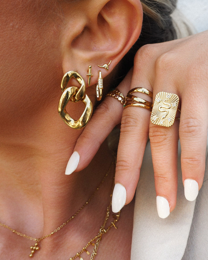 Close up of a woman's ear and hand with gold jewelry