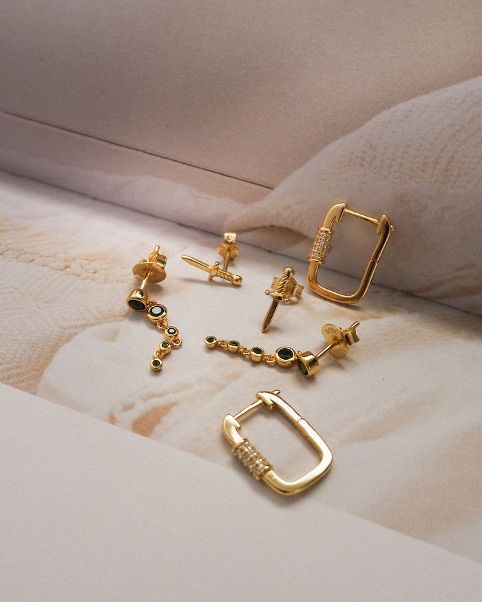 Three pairs of gold accent earrings on a neutral background