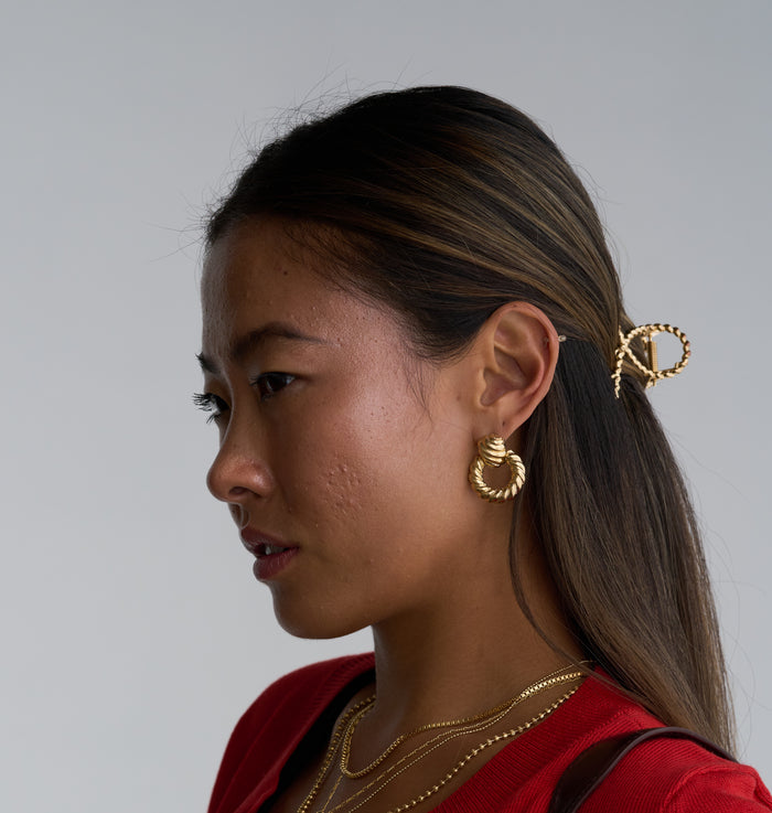 A woman wearing gold jewelry and a red cardigan on a white background