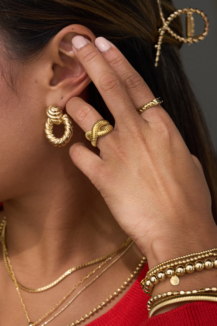 A woman with gold jewelry holding her hand up to her face
