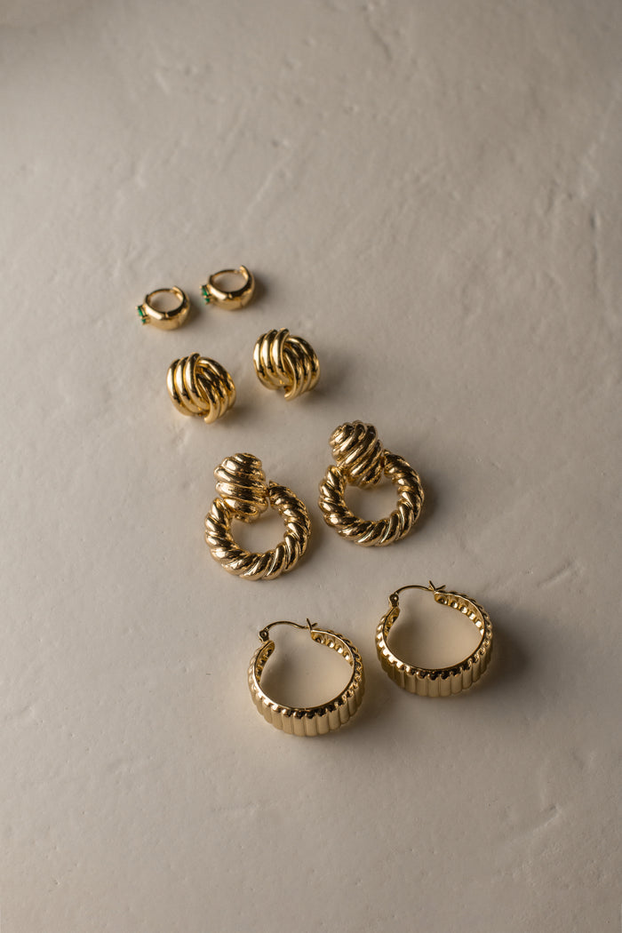 Four pairs of gold earrings on a neutral stone background
