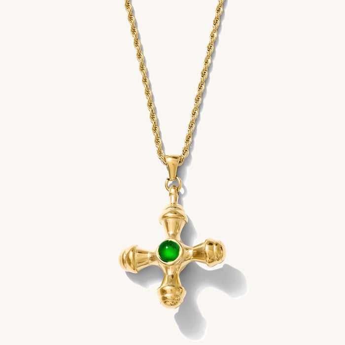 Close up of the gold Dune necklace with an emerald center stone on a white background