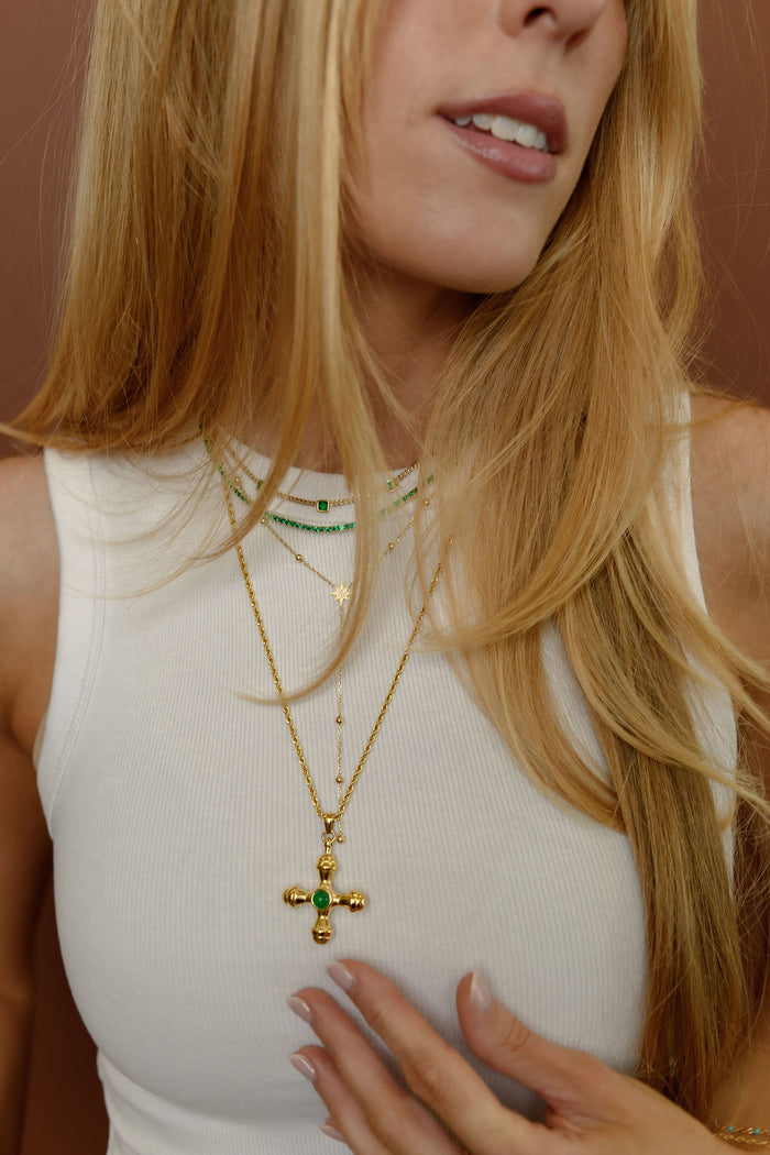 Detail view of the gold Dune necklace with an emerald center stone on a white background