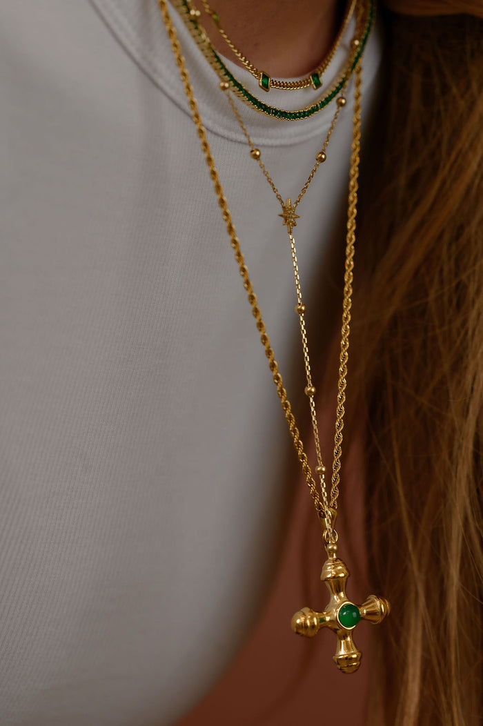 Studio close up of the gold Dune necklace with an emerald center stone on a white background