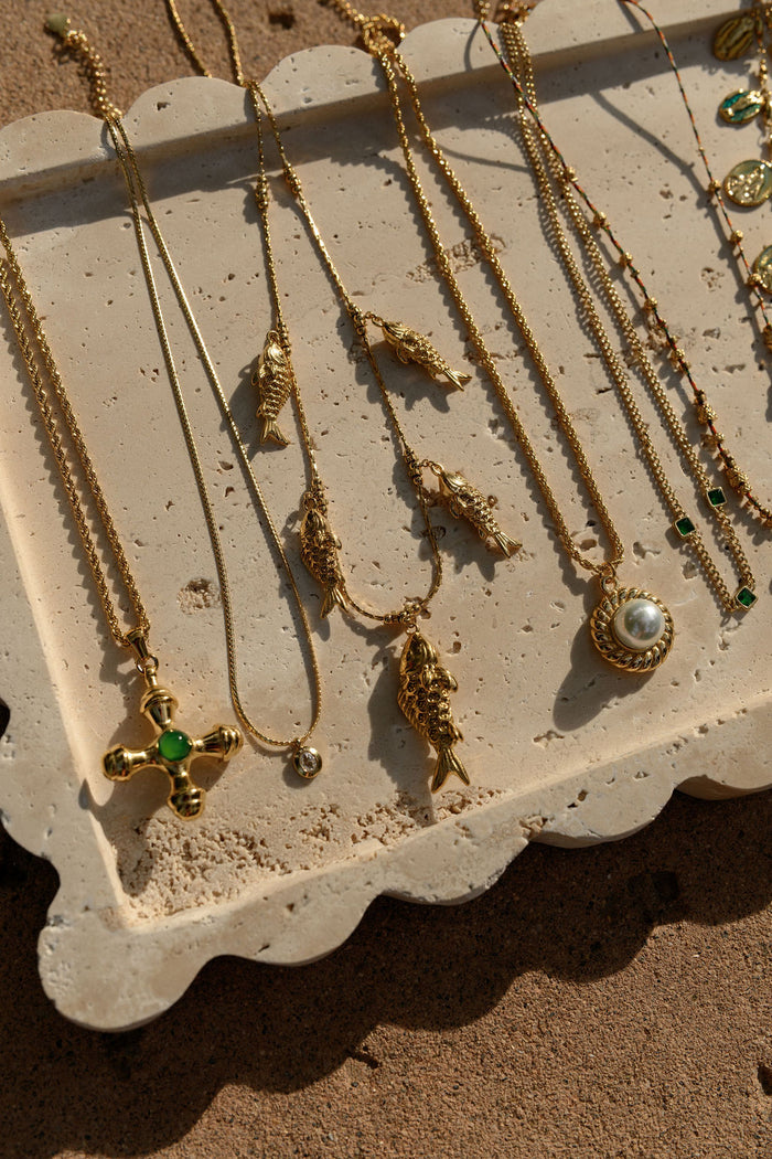 Close up of the gold Dune necklace with an emerald center stone by Beads by Tara on a white background
