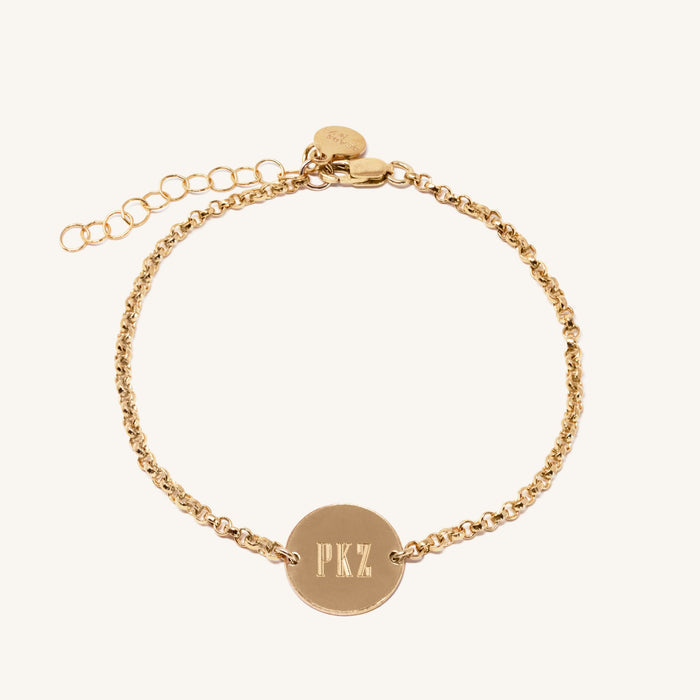 Close up of a gold chain bracelet with engraved circle tag on a white background