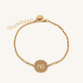 Close up of a gold chain bracelet with engraved circle tag on a white background