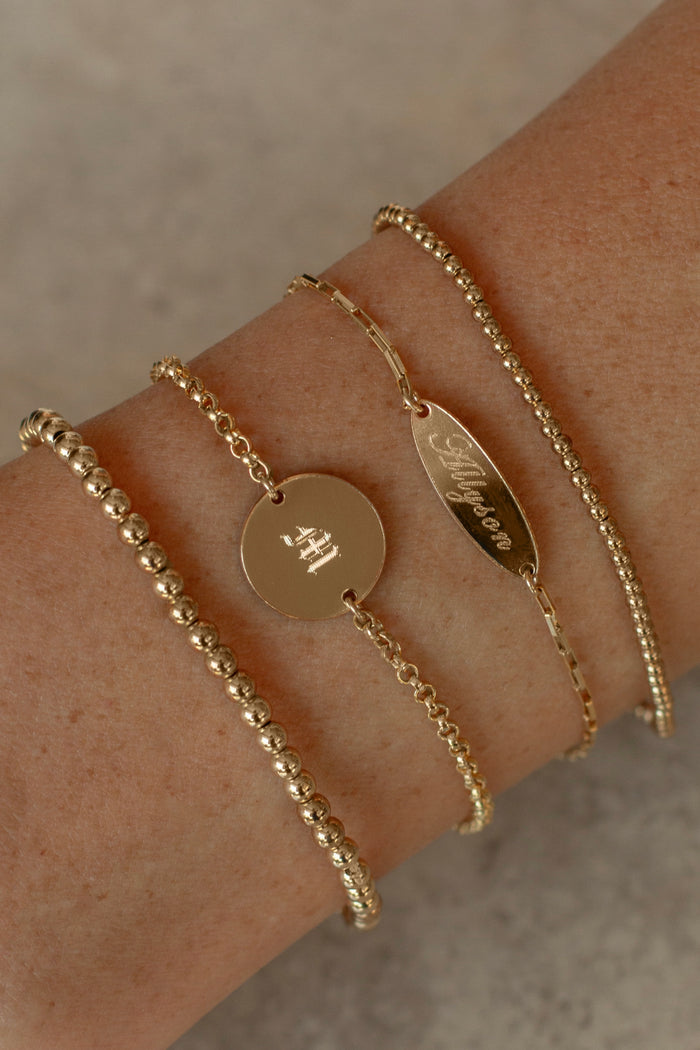 A wrist with simple gold bracelets on a taupe background