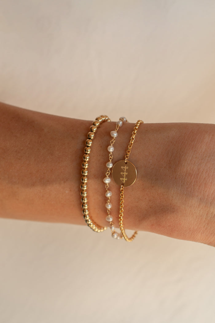 A wrist with dainty gold bracelets on a neutral background