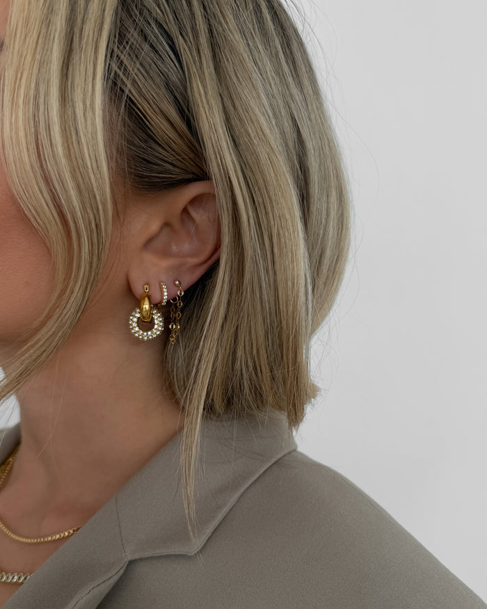A woman wearing gold and stone earrings on a white background
