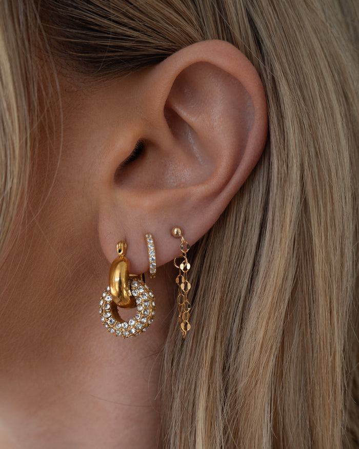 Close-up of an ear with multiple gold and crystal earrings