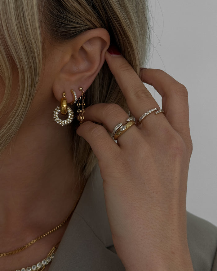 Close-up of an ear with multiple gold and crystal earrings